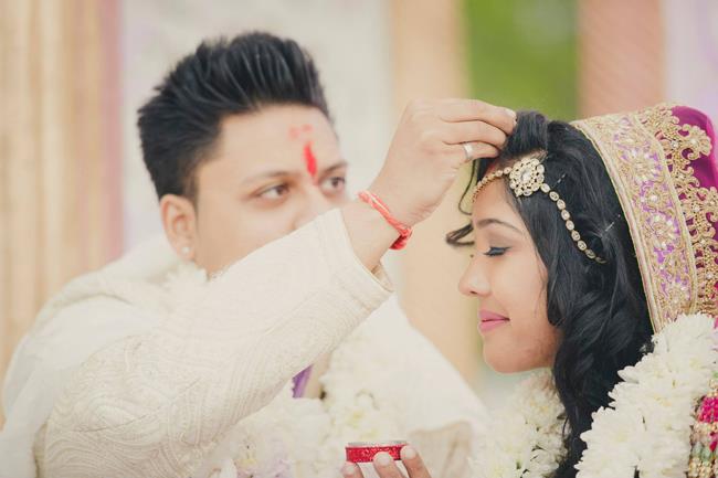 Indian groom applying sindoor on bride in Hindu wedding